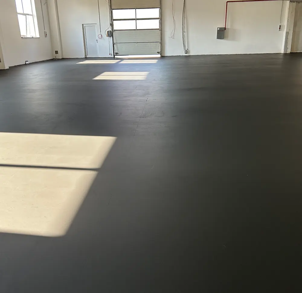 Dekoratív kezelt estrich beton padló tágas ipari belső térben, matt sötét felülettel és természetes fényben