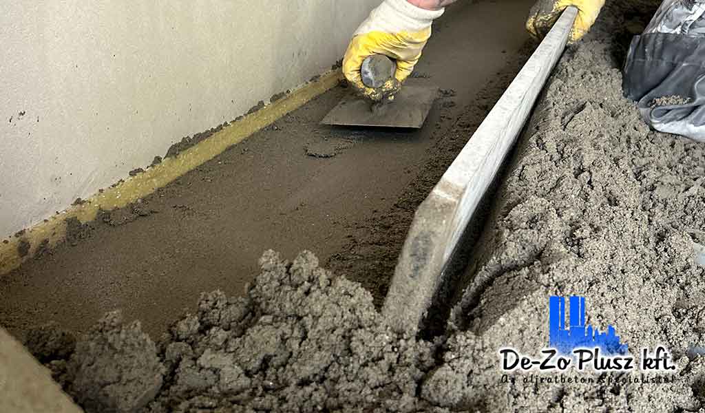 Szakember estrich beton simítás közben, simítóval és szintezőléccel, jól látható peremszigeteléssel – aljzatkiegyenlítés folyamata.